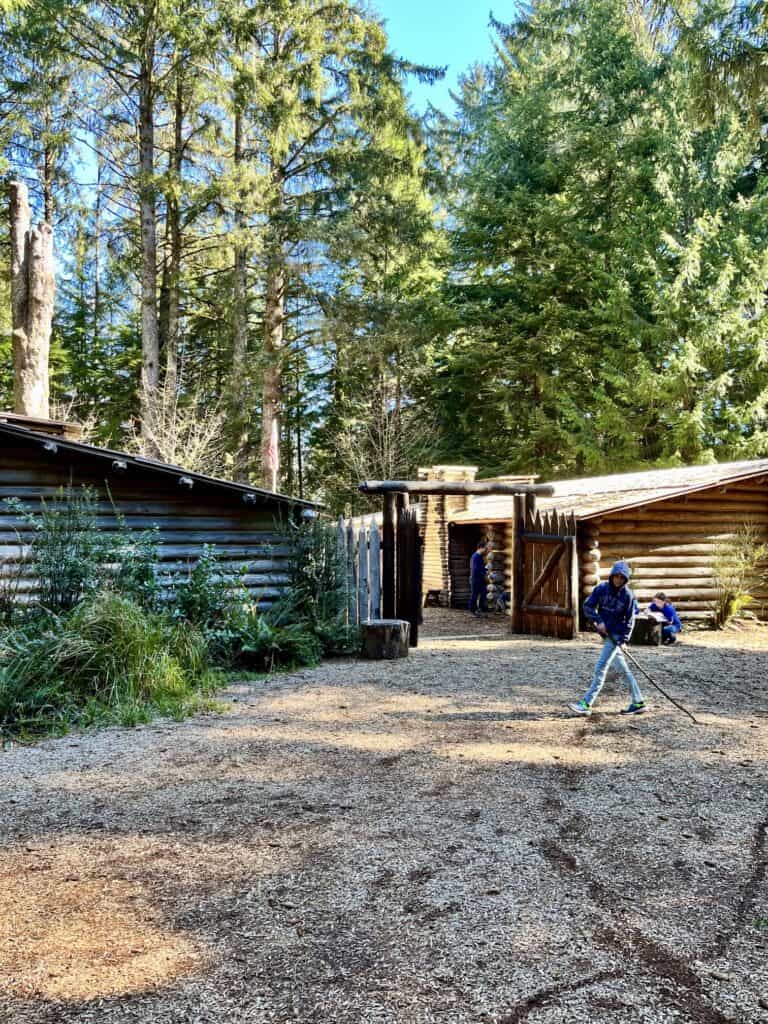 Our son draws in the ground with a stick in front of the replica Fort Clatsop. One day in Astoria Oregon with kids.