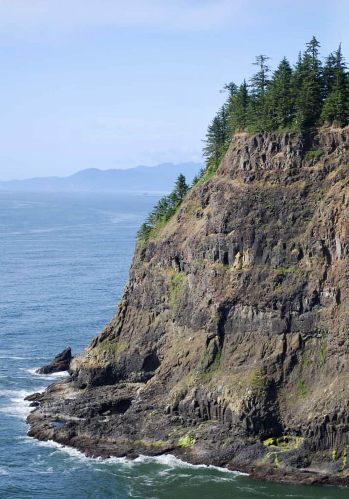 A forested, rocky headland towers over the ocean at Cape Meares State Scenic Viewpoint.