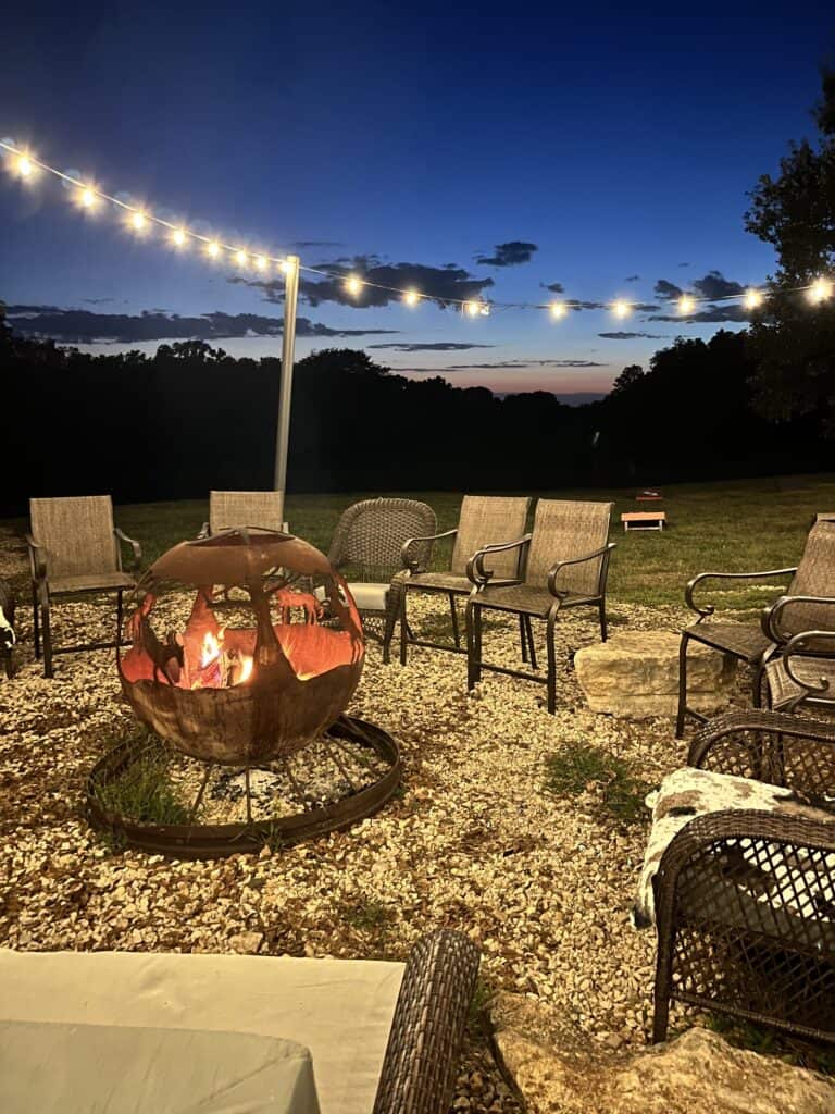 The fire pit surrounded by comfy chairs and twinkle lights.