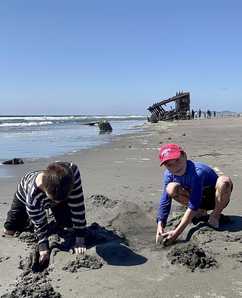 Our son smiles as he and his brother play at the beach at Fort Stevens State Park. The shipwreck of the Peter Iredale stands in the distance.