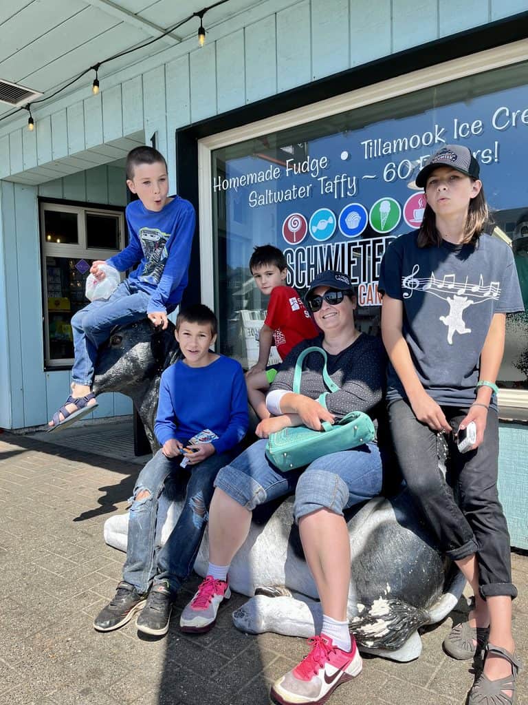 My wife and children smile on a cow-shaped bench that sits in front of a store at Rockaway Beach, Oregon.