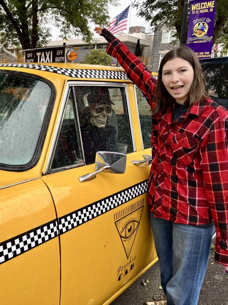Our daughter in a red flannel shirt and jeans poses next to Benny the cab driver from the Halloweentown movie
