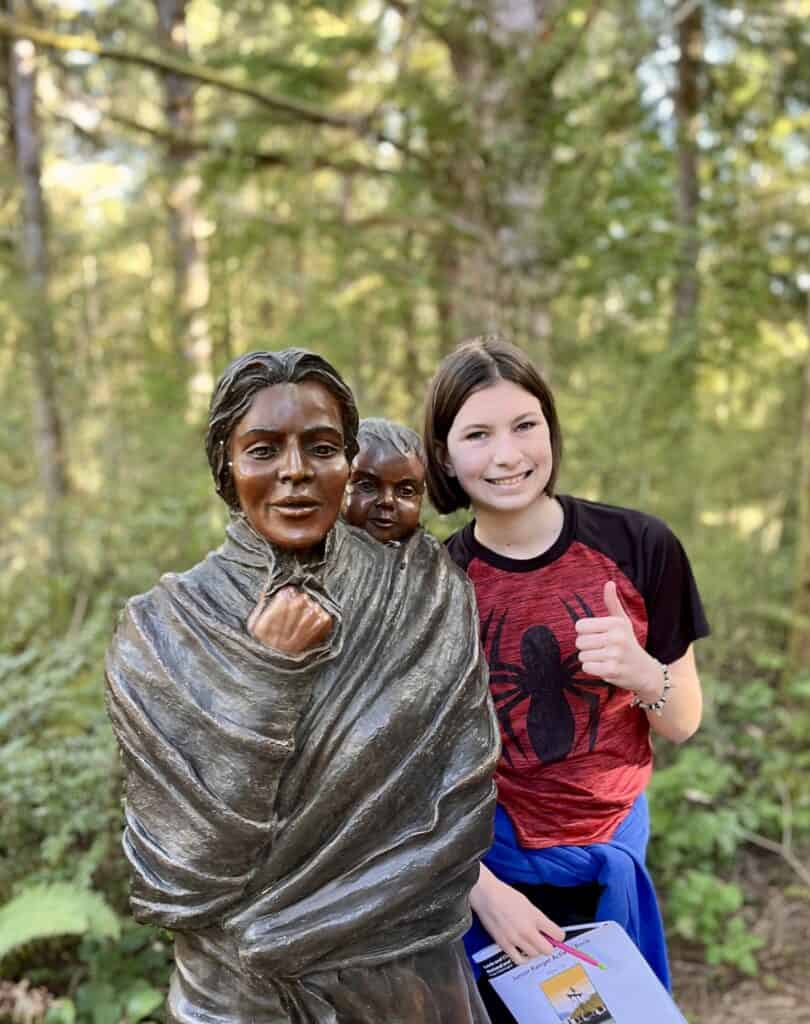 Our daughter smiles and poses beside a statue of Sacagawea and Pompey at Lewis & Clark National Historical Park.