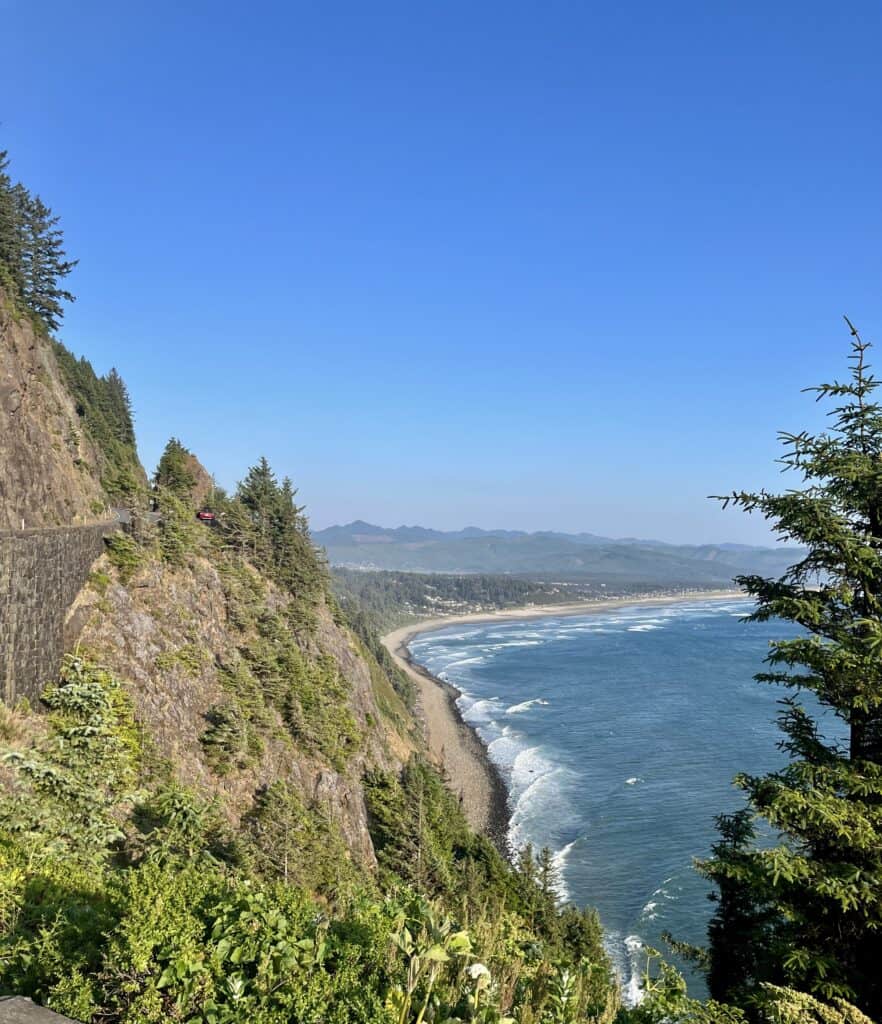 Basalt bluffs tower over the surf and sand at the Neahkahnie Viewpoint. Manzanita Beach and the Coastal Range can be seen far off in the distance.