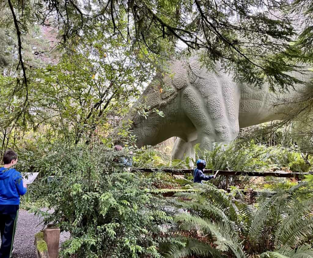 A dinosaur sculpture towers over our children as they explore at Prehistoric Gardens.
