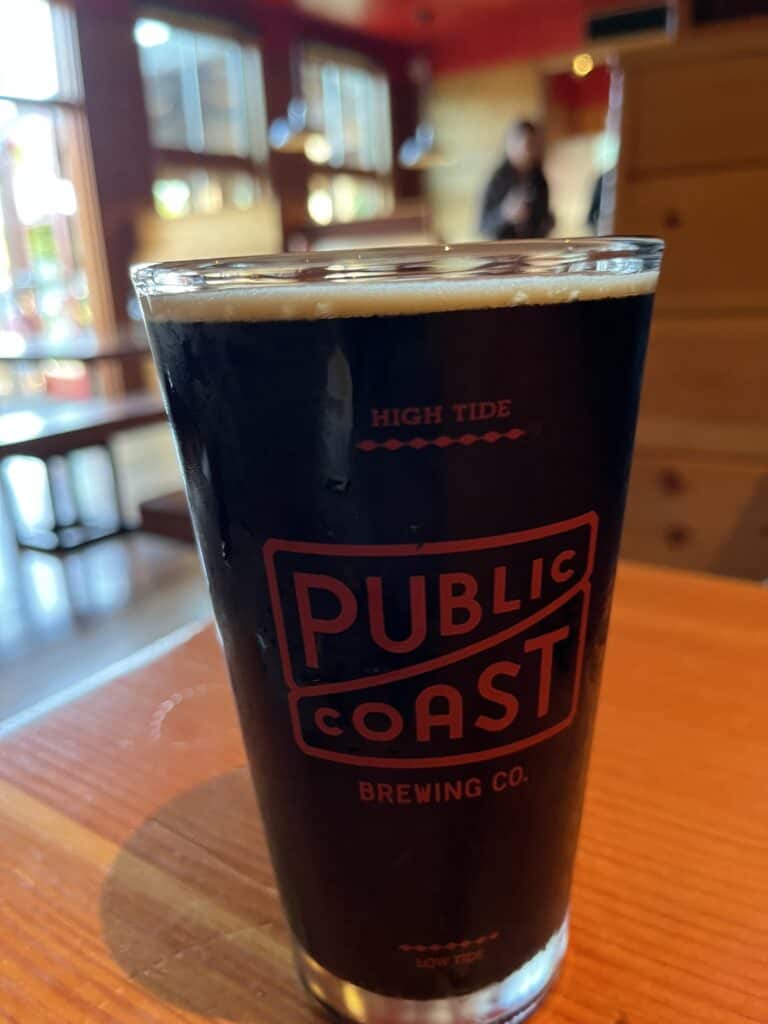 A full glass of dark beer sits on a table at Public Coast Brewing Company.