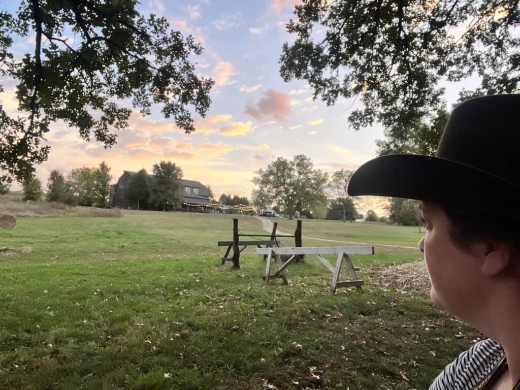 Jenn wearing cowboy hat looking towards the inn building at dawn.