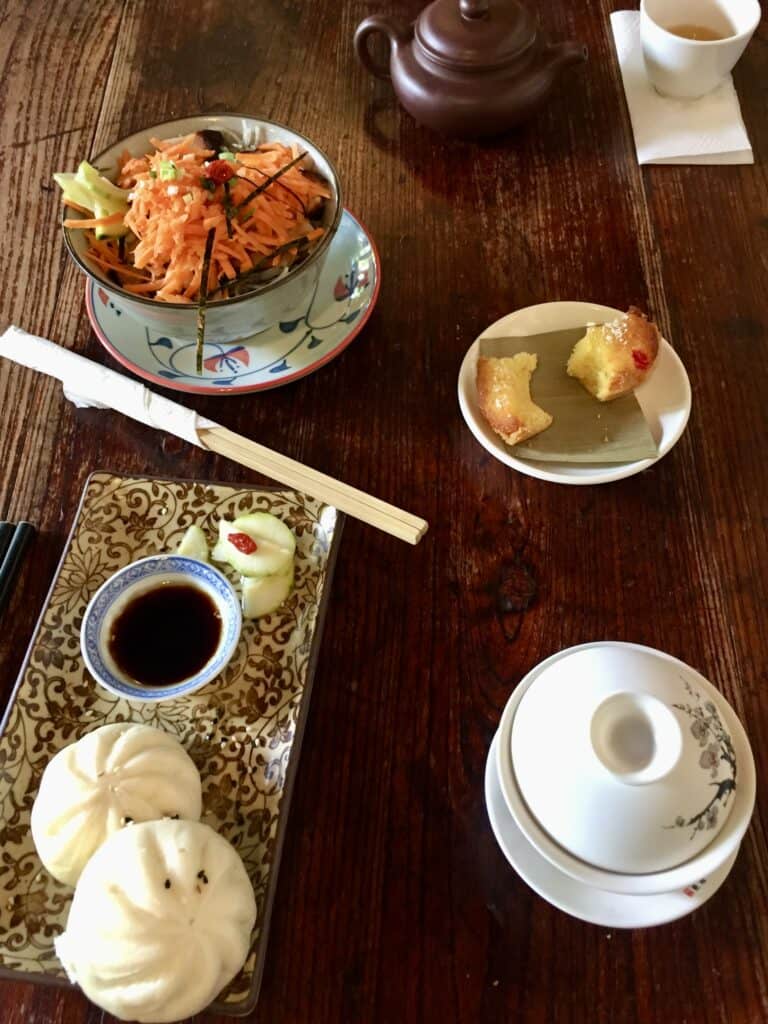 Traditional Chinese food on a table including chopsticks, buns, and tea cup.
