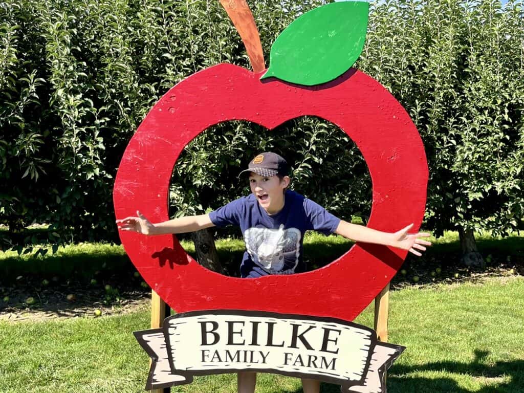 Our son in a wooden apple cutout with the Beilke Family Farm sign below.