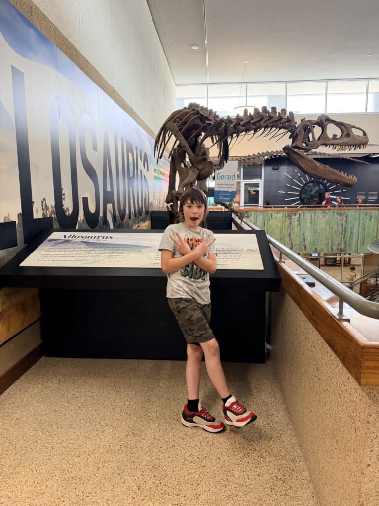 Our son poses in front of the Allosaurus skeleton model.
