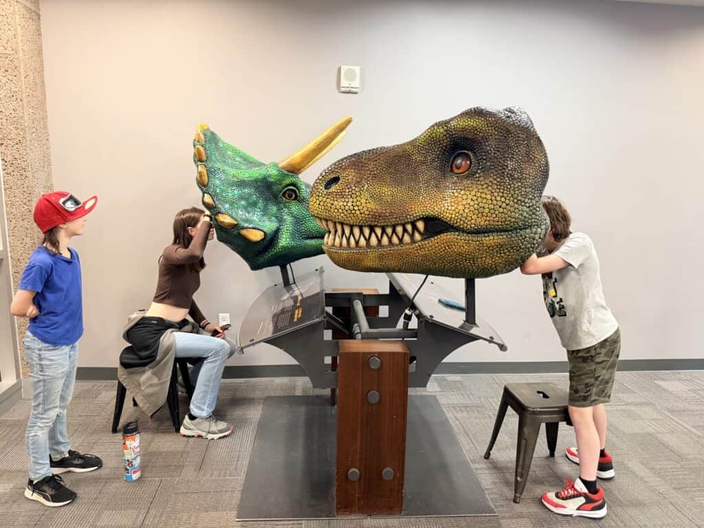 Our kids stick their faces inside giant dinosaur masks.