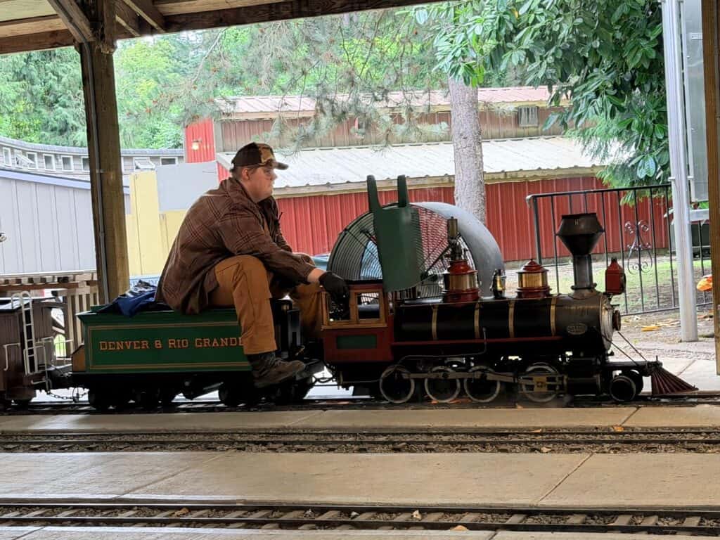 Volunteer sitting behind a miniature steam locomotive at the Molalla Train Park.
