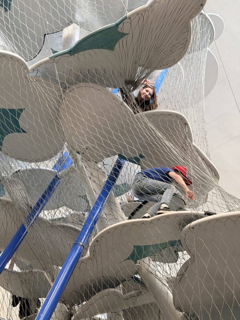 Our teen daughter gives the peace sign as her brother climbs on a lower level on the Cloud Climber.